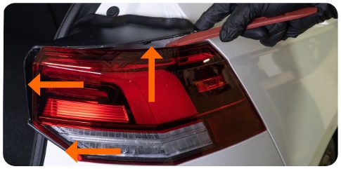 Pry tool at the outer tail light bezel of a MK8 Golf with three arrows marking the release points