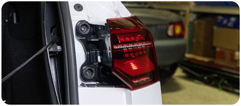 New Euro outer tail light being offered up to the quarter panel of a MK8 Golf with the two bolt bosses visible