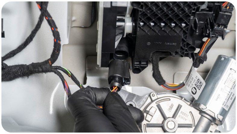 Gloved hand disconnecting the plug from the rear view camera module inside the hatch of a MK8 Golf